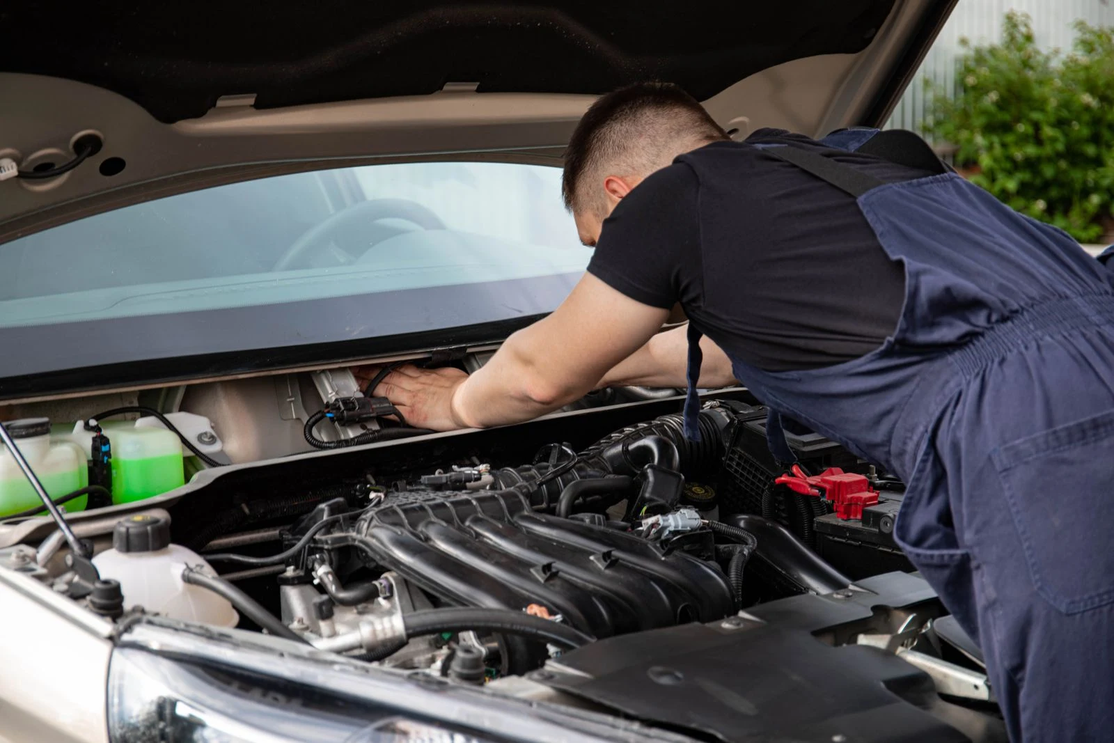 Mechaniker in Arbeitskleidung beugt sich über den geöffneten Motorraum eines Fahrzeugs
